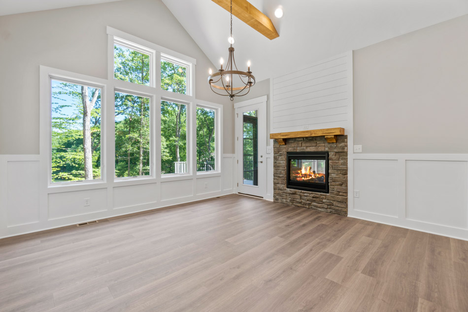 A home interior with wide windows, giving great illumination, a fireplace with stone surround and a wall-mounted wood shelf