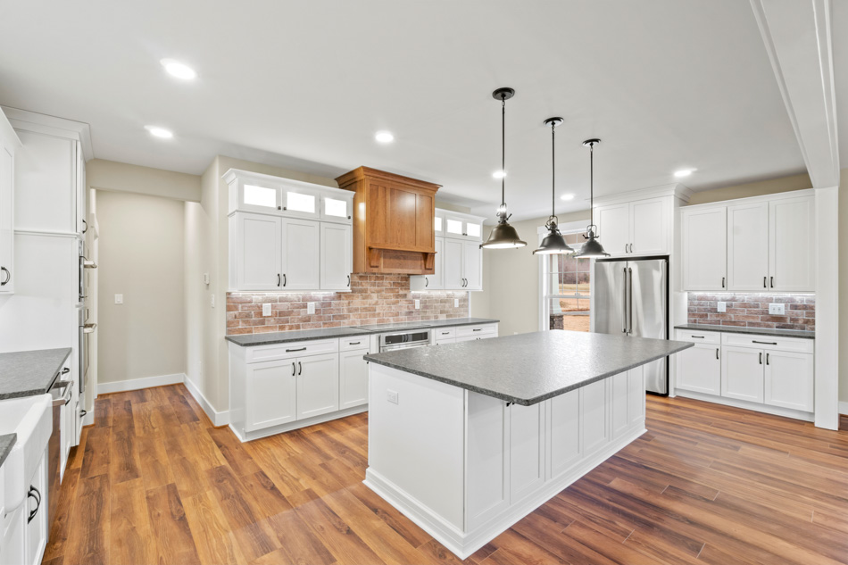 A remodeled kitchen with U-shaped design, and an island with hanging light fixtures, cabinets with recessed lights, a tile with brick-looking backsplash, and hardwood floors